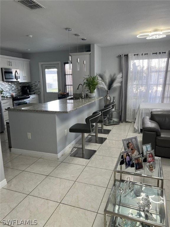 kitchen featuring backsplash, light tile flooring, white cabinets, sink, and pendant lighting