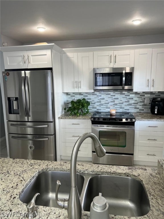 kitchen with sink, tasteful backsplash, white cabinetry, stainless steel appliances, and light stone countertops