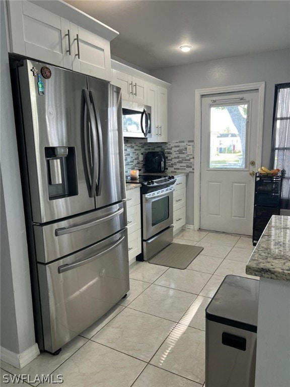 kitchen with appliances with stainless steel finishes, light tile floors, tasteful backsplash, white cabinetry, and light stone countertops