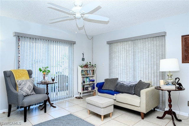 living area featuring a textured ceiling, light tile patterned flooring, a ceiling fan, and baseboards