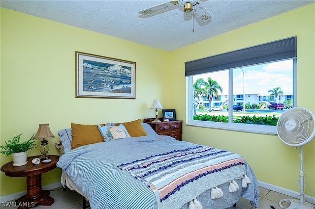 bedroom featuring a ceiling fan, a textured ceiling, baseboards, and light tile patterned floors