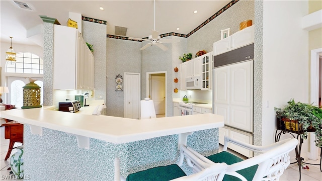 kitchen with kitchen peninsula, a kitchen breakfast bar, white appliances, light tile patterned floors, and white cabinetry