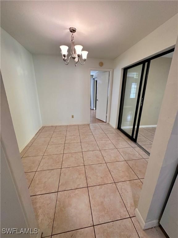 tiled spare room featuring a chandelier