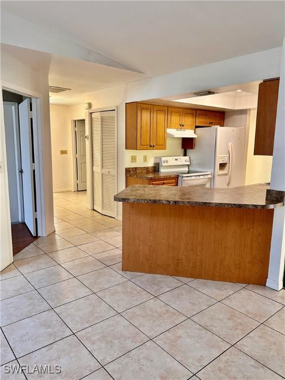 kitchen featuring light tile patterned floors, white appliances, and kitchen peninsula