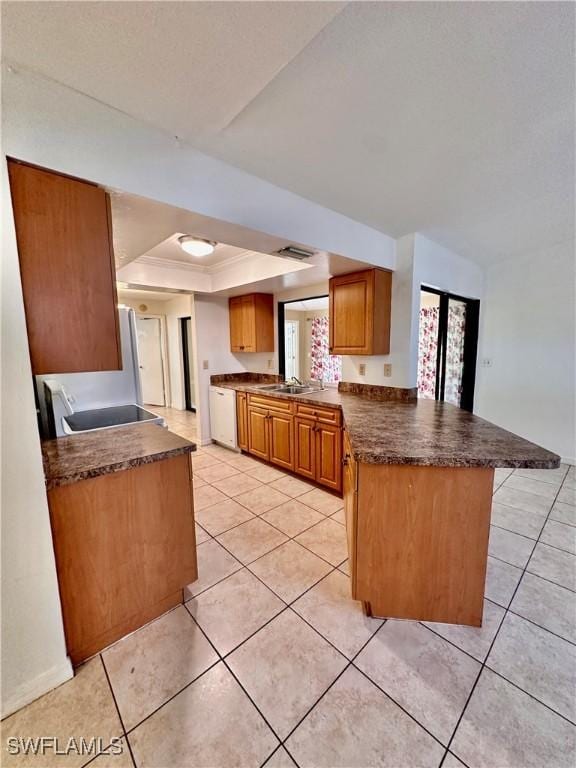 kitchen featuring range, light tile patterned floors, a tray ceiling, white dishwasher, and kitchen peninsula