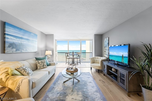 living room with a water view, a textured ceiling, a wall of windows, and light wood-type flooring