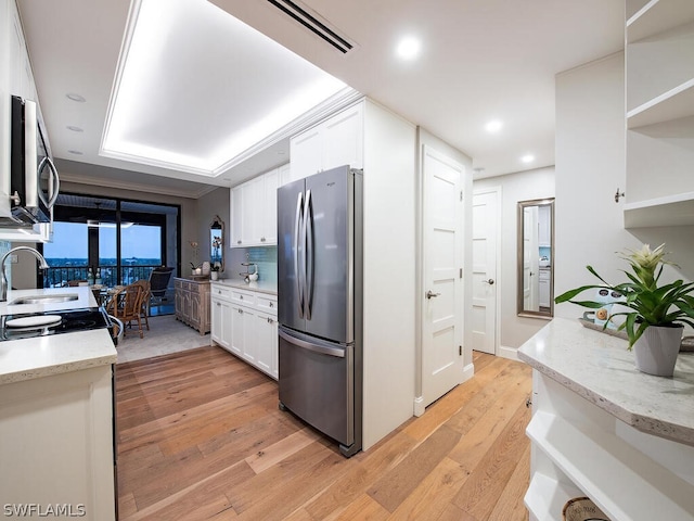 kitchen with light stone countertops, white cabinetry, light hardwood / wood-style floors, a tray ceiling, and appliances with stainless steel finishes