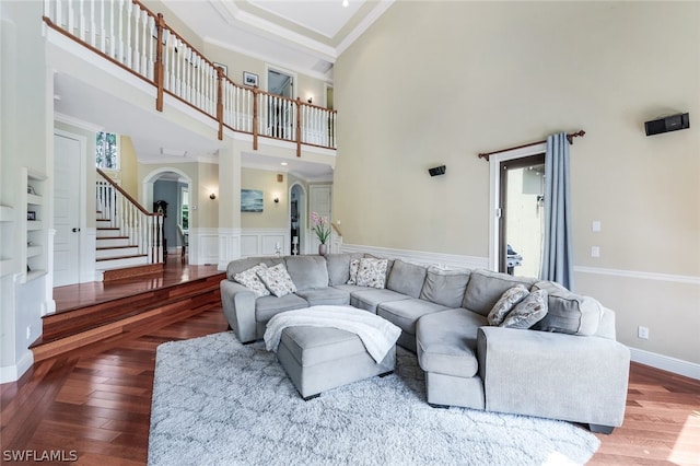 living room featuring hardwood / wood-style flooring, built in features, ornamental molding, and a high ceiling