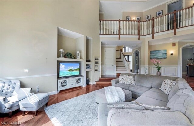 living room featuring a towering ceiling, hardwood / wood-style flooring, built in features, and ornamental molding