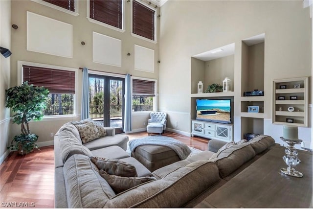 living room with hardwood / wood-style floors, a towering ceiling, and built in shelves