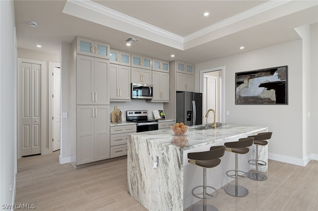 kitchen with a kitchen breakfast bar, a kitchen island with sink, appliances with stainless steel finishes, sink, and a raised ceiling