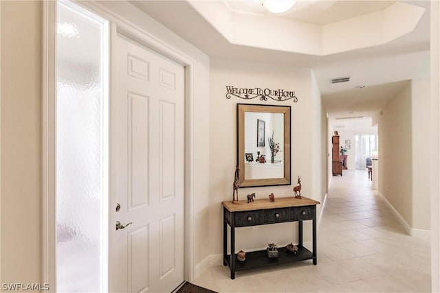 hallway featuring a tray ceiling, light tile patterned flooring, visible vents, and baseboards