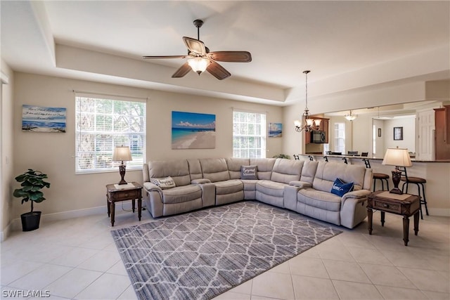 living area featuring a tray ceiling, a healthy amount of sunlight, baseboards, and light tile patterned floors