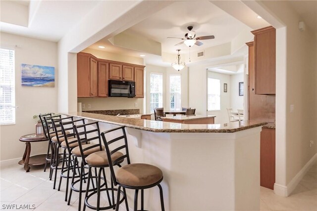 kitchen featuring a peninsula, black microwave, dark stone counters, and a tray ceiling