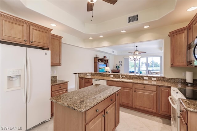 kitchen with white appliances, a sink, a kitchen island, visible vents, and a raised ceiling