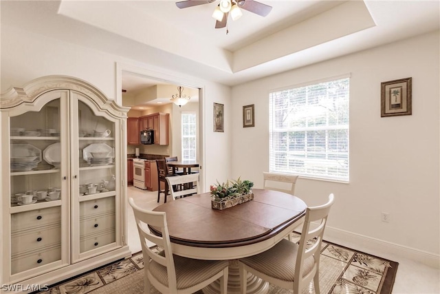 dining area featuring a tray ceiling, a ceiling fan, a wealth of natural light, and baseboards