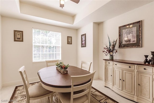 dining area with light tile patterned floors, a tray ceiling, a ceiling fan, and baseboards