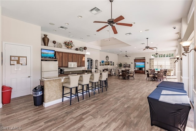 kitchen with white appliances, visible vents, open floor plan, light wood finished floors, and a kitchen bar