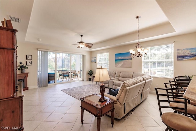 living area with a tray ceiling, visible vents, a glass covered fireplace, and light tile patterned floors