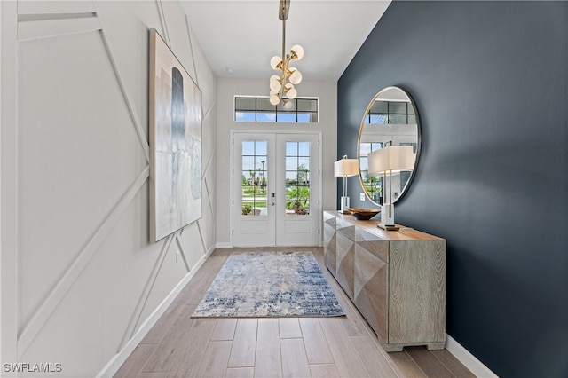 foyer with light wood-type flooring, a high ceiling, baseboards, and french doors