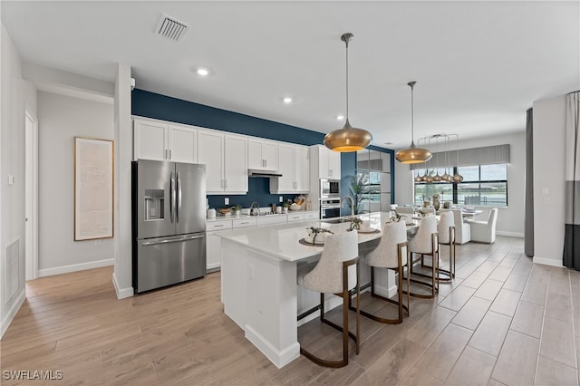 kitchen with a kitchen island with sink, white cabinetry, a breakfast bar area, and appliances with stainless steel finishes