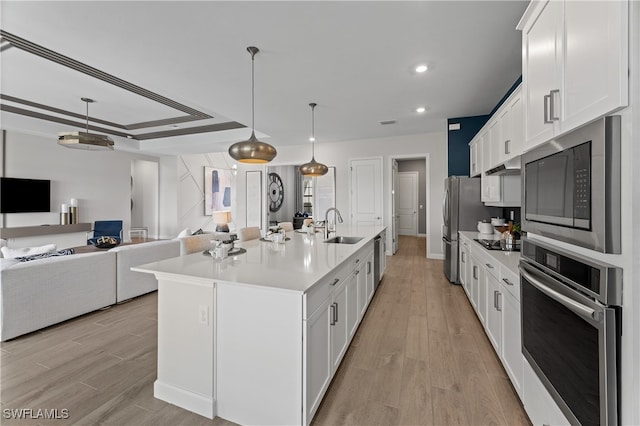 kitchen with appliances with stainless steel finishes, sink, light hardwood / wood-style floors, an island with sink, and white cabinetry