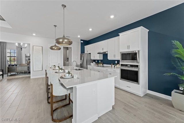 kitchen with white cabinetry, light hardwood / wood-style floors, appliances with stainless steel finishes, a kitchen breakfast bar, and a center island with sink