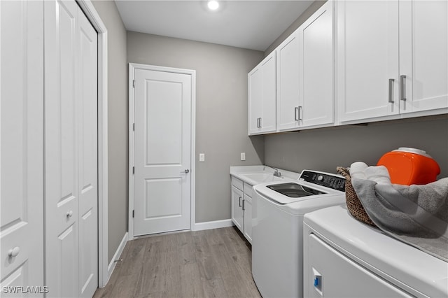 laundry area with washer and clothes dryer, cabinet space, light wood-style flooring, a sink, and baseboards