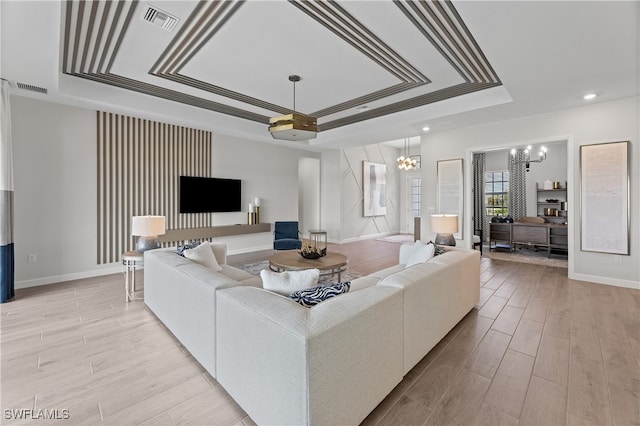 living room featuring a chandelier, light hardwood / wood-style flooring, and a tray ceiling