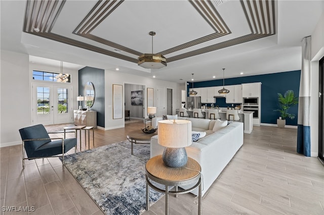 living area featuring light wood-style floors, a tray ceiling, french doors, and baseboards