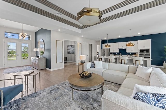 living room with a tray ceiling, ornamental molding, sink, french doors, and light hardwood / wood-style flooring