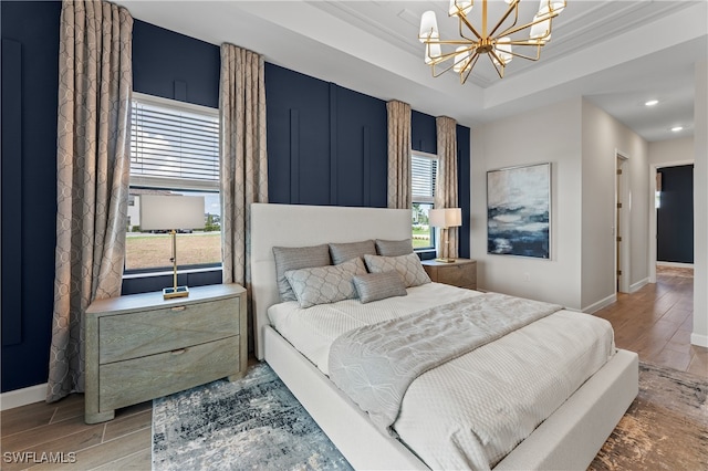 bedroom featuring multiple windows, wood-type flooring, a chandelier, and a tray ceiling