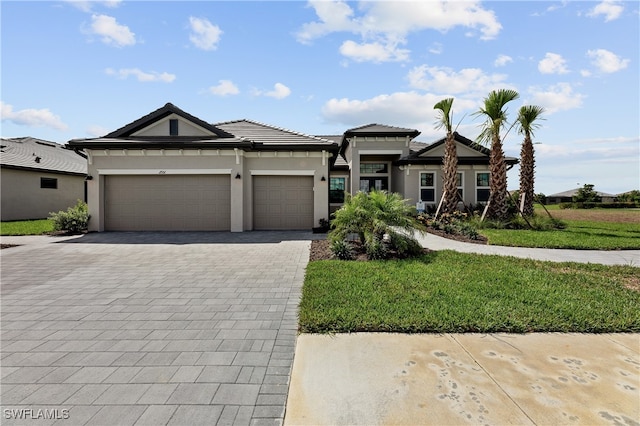 prairie-style house with a garage, a tile roof, decorative driveway, stucco siding, and a front yard