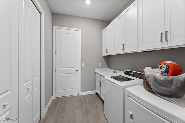 laundry area featuring sink, independent washer and dryer, light wood-type flooring, and cabinets