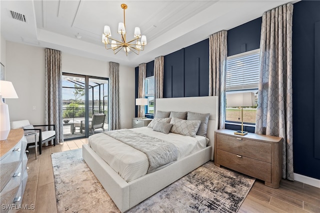 bedroom with an inviting chandelier, access to outside, light hardwood / wood-style flooring, and a raised ceiling