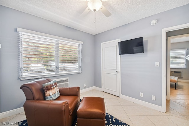 sitting room with light tile patterned floors, a textured ceiling, an AC wall unit, and ceiling fan