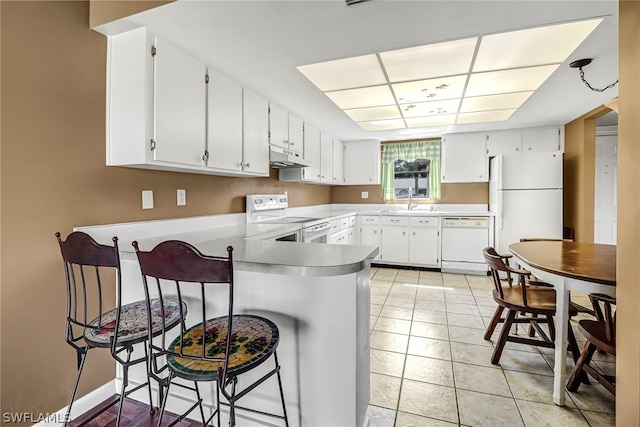 kitchen featuring light tile floors, a kitchen bar, white appliances, white cabinetry, and kitchen peninsula