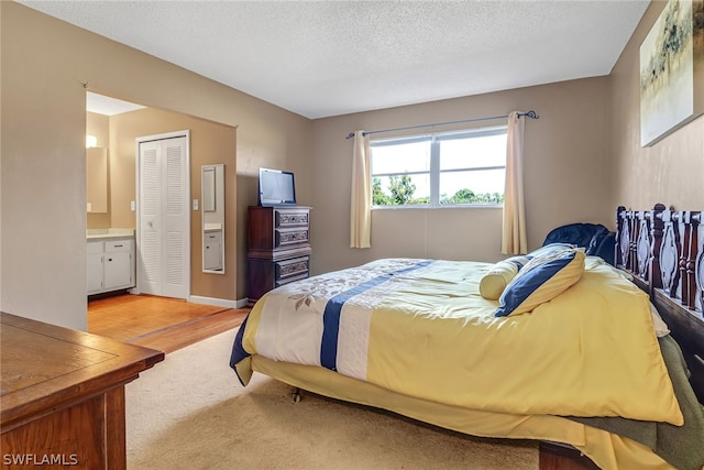 bedroom featuring light hardwood / wood-style floors, ensuite bathroom, and a textured ceiling