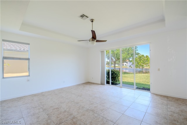 unfurnished room featuring a raised ceiling, ceiling fan, and light tile floors