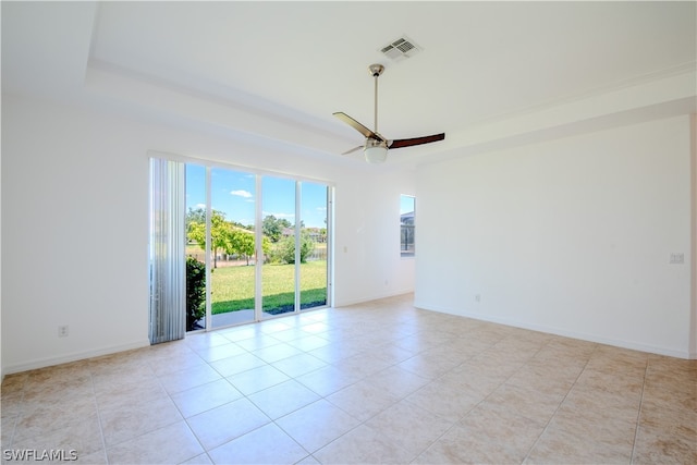 unfurnished room featuring a raised ceiling, ceiling fan, and light tile floors