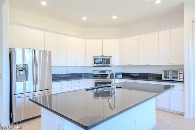 kitchen featuring dark stone countertops, stainless steel appliances, white cabinets, and a center island with sink