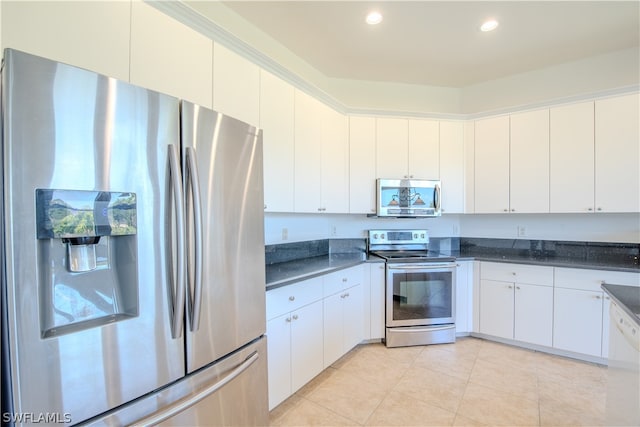 kitchen with appliances with stainless steel finishes, dark stone countertops, light tile floors, and white cabinetry