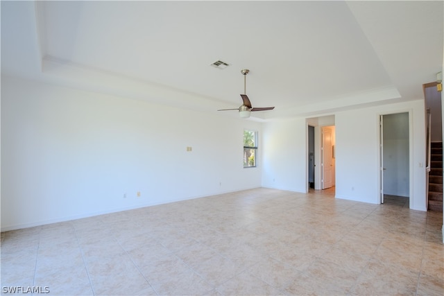 tiled empty room with ceiling fan and a raised ceiling