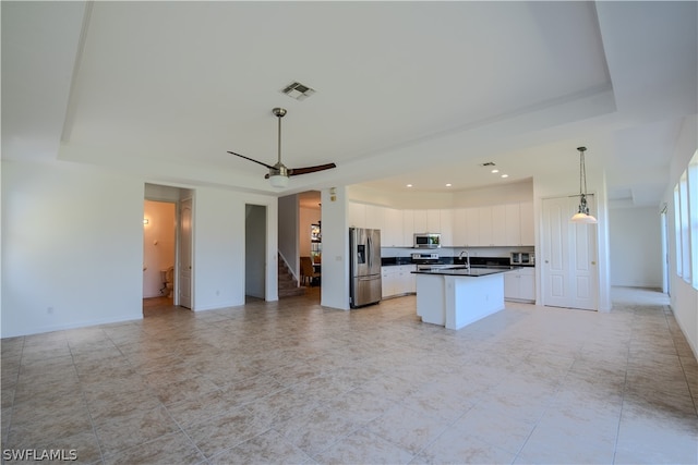 kitchen with hanging light fixtures, stainless steel appliances, light tile floors, ceiling fan, and an island with sink