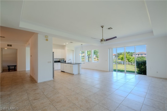 unfurnished living room with sink, ceiling fan, a raised ceiling, and light tile flooring