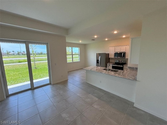 kitchen with kitchen peninsula, appliances with stainless steel finishes, light stone counters, sink, and white cabinets