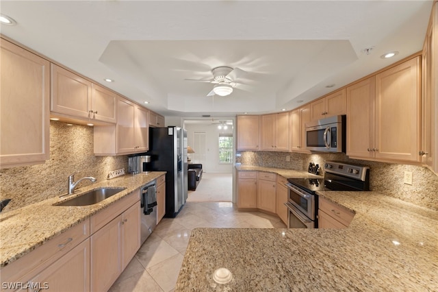 kitchen with sink, light stone countertops, light brown cabinetry, appliances with stainless steel finishes, and a tray ceiling