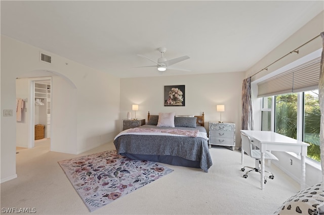 bedroom with ceiling fan, a walk in closet, light carpet, and multiple windows