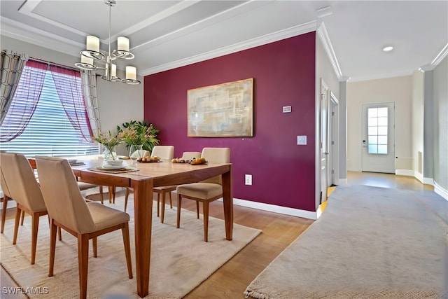 dining space with ornamental molding, a raised ceiling, an inviting chandelier, and light wood-type flooring