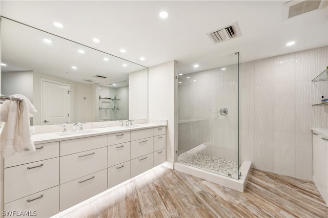 bathroom featuring tiled shower, vanity with extensive cabinet space, hardwood / wood-style flooring, and dual sinks